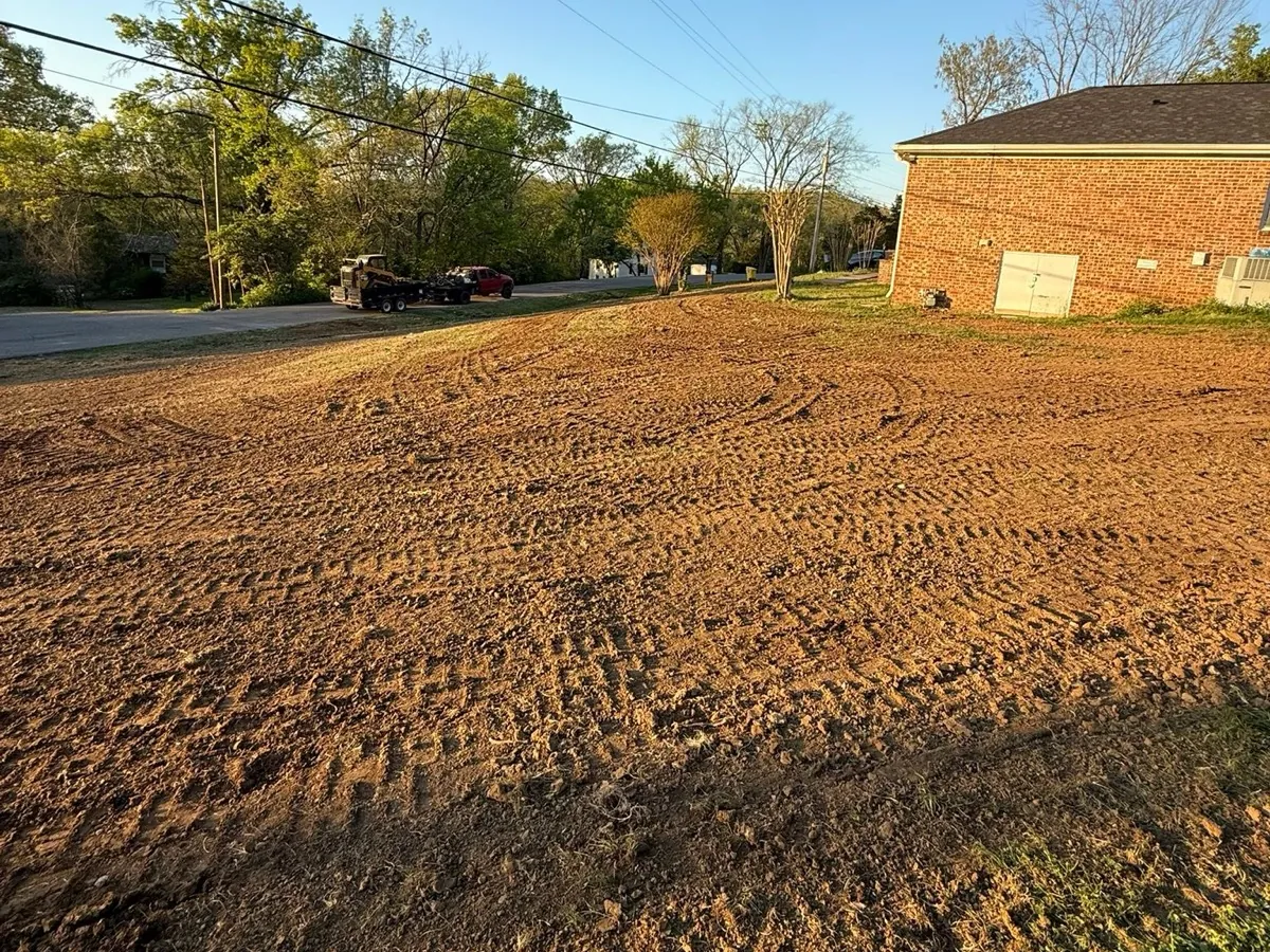 Freshly graded bare soil across a side yard after septic work, beside a brick house
