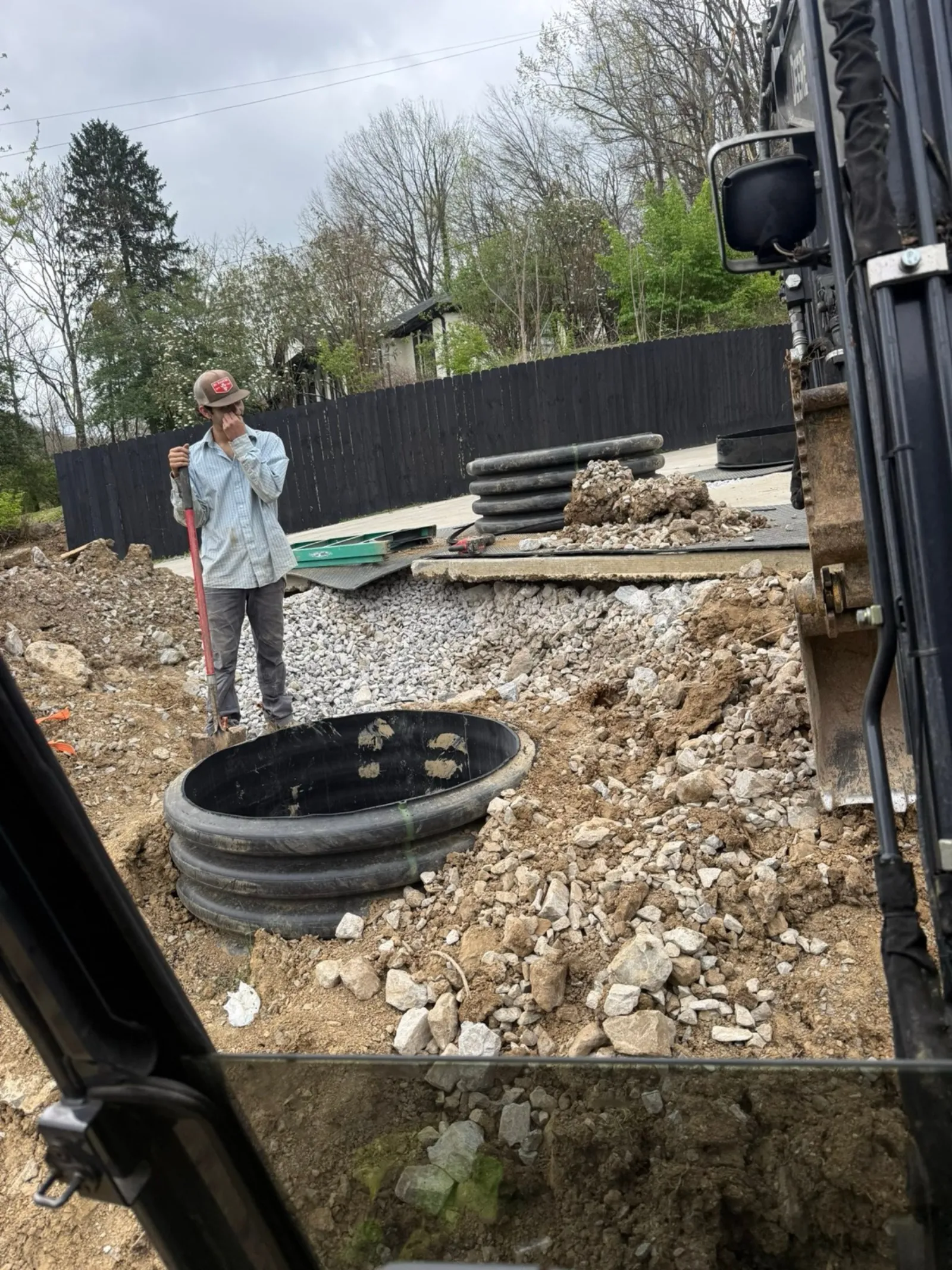 Black plastic septic tank risers stacked beside a gravel work area before installation