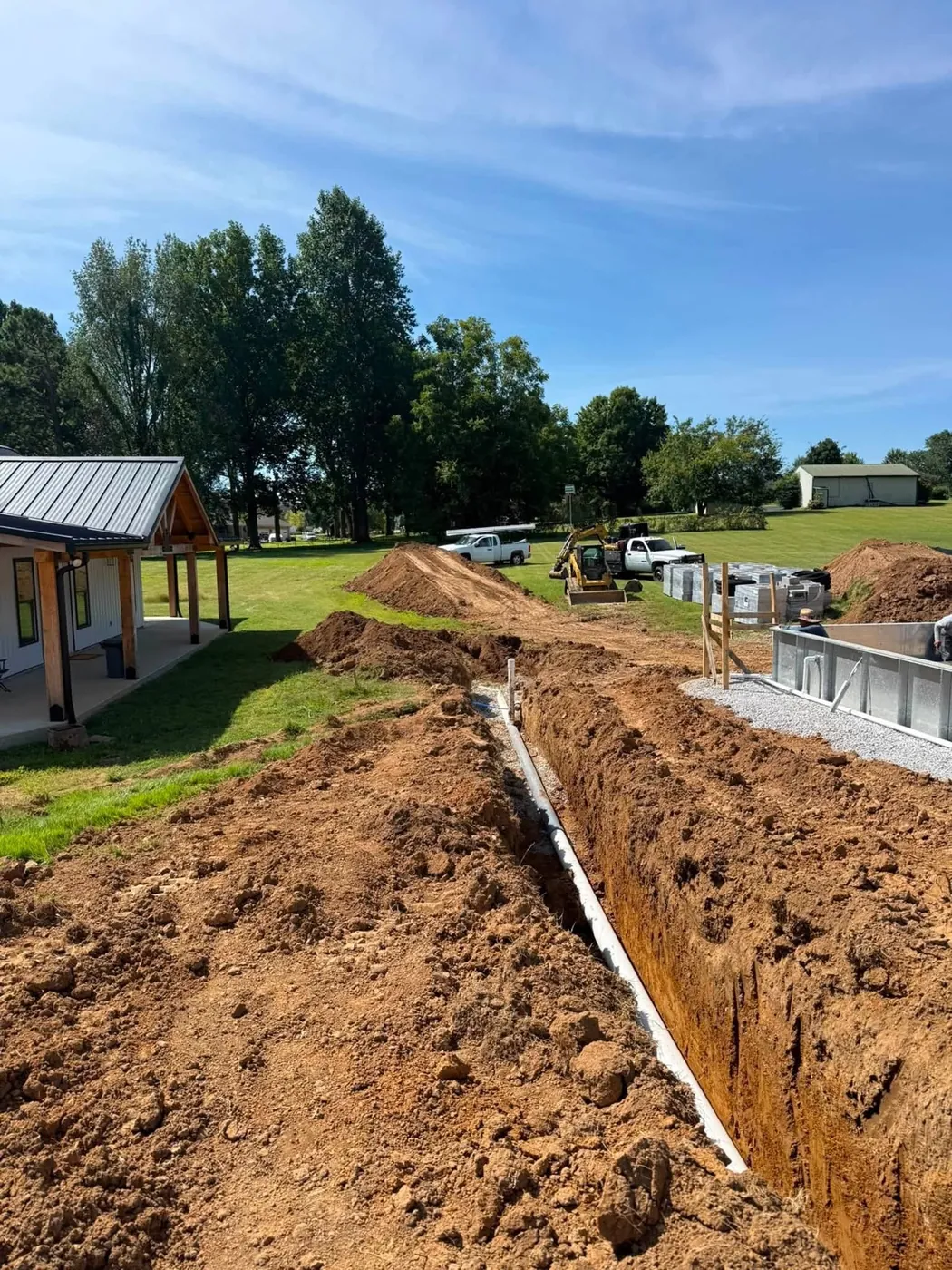 Long open trench with white pipe running beside a new building